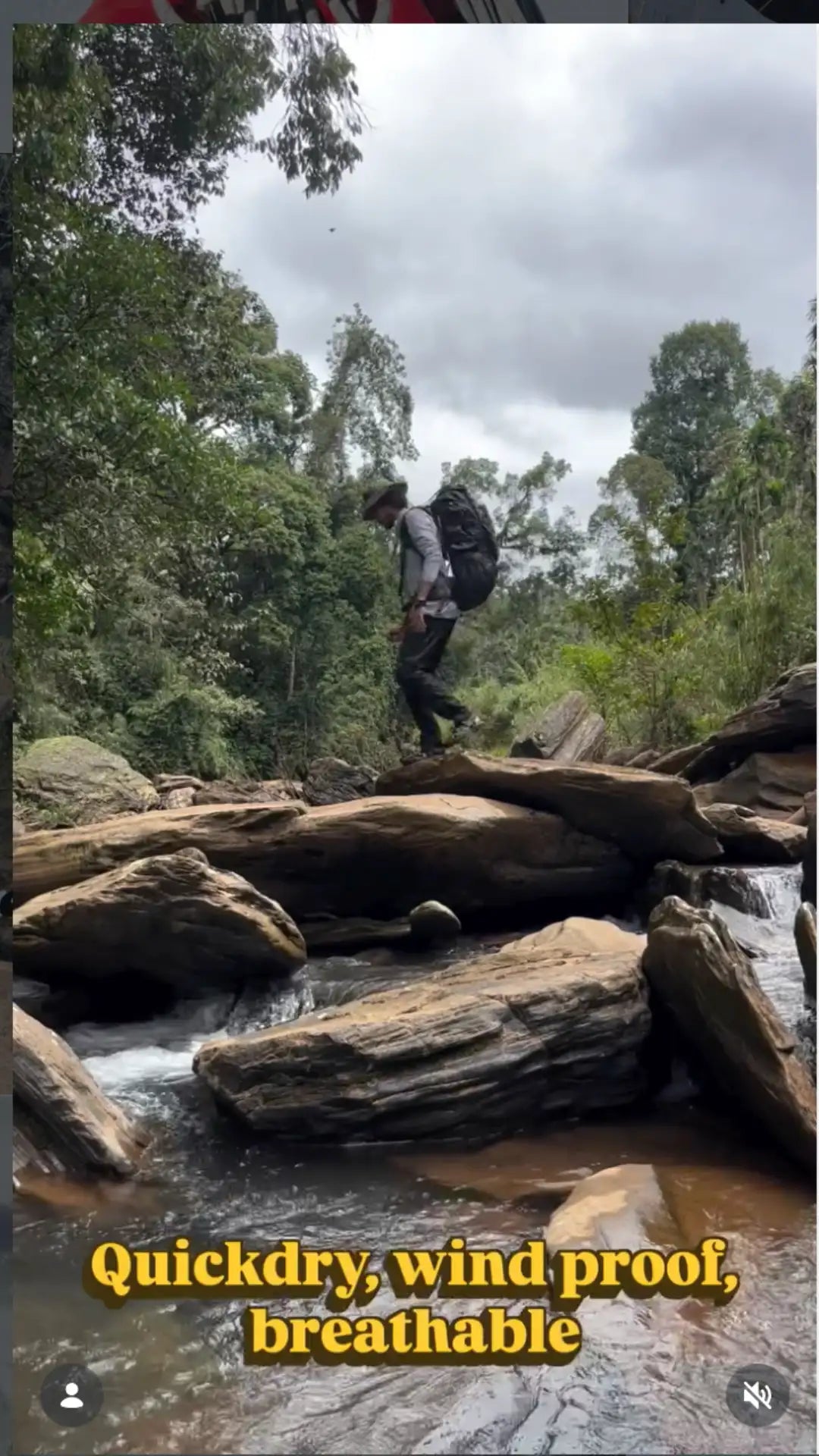 Black backpack worn by a hiker crossing rocky streambed