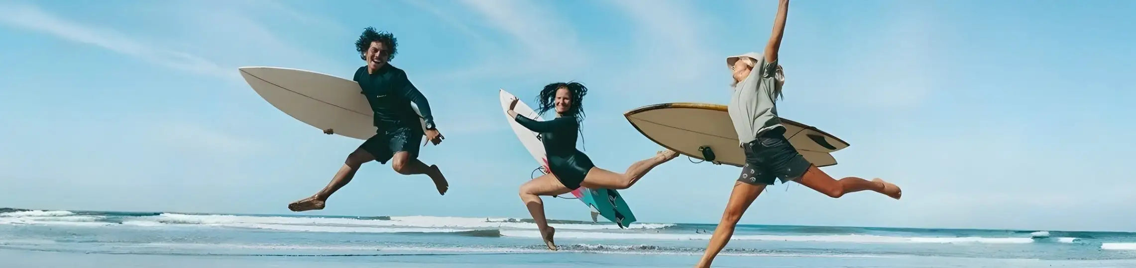 Three surfers in athletic wear leap mid-air with their surfboards, each displaying a unique style and color scheme.
