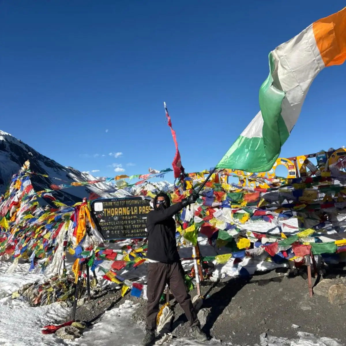 A vibrant green, white, and orange flag waving in the wind at a high-altitude mountain pass.