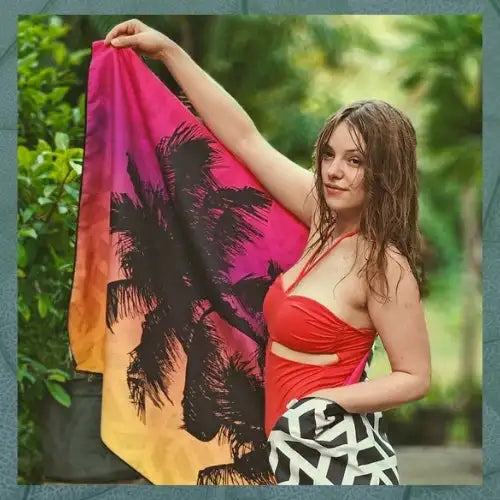 A vibrant pink, orange and yellow gradient beach towel featuring bold black palm tree silhouettes.